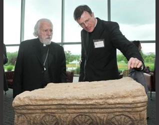 El P. Eamon explica los detalles en una réplica de la piedra esculpida de Magdala a Su Eminencia Isaiah, Metropolita de los ortodoxos griegos de Denver.